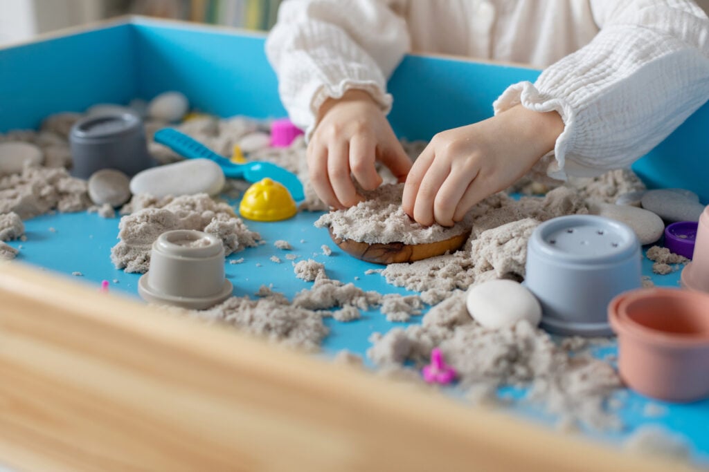 Children activity with kinetic sand for motor and sensory development. Toddler hands play therapy with colorful toys on sandbox.