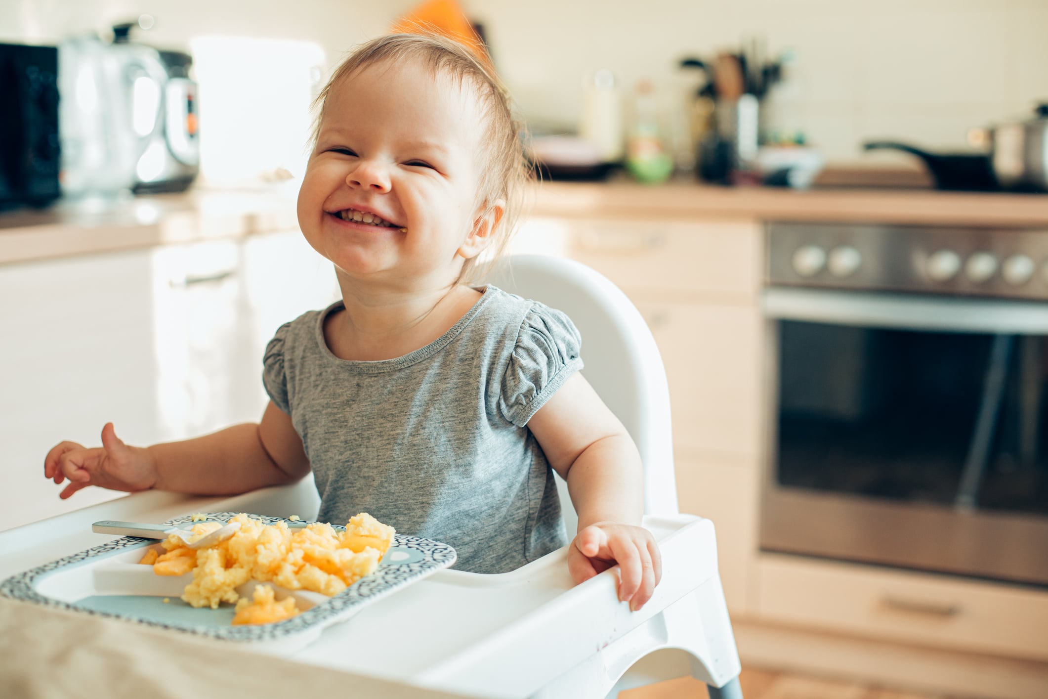 Cute toddler sitting on baby highchair and smiling with her teeth revealed